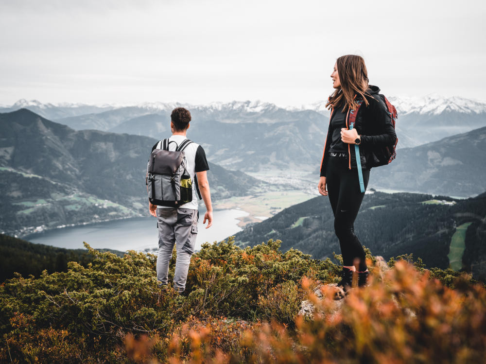 Zwei Wanderer stehen auf der Schmittenhöhe bei Zell am See und blicken auf den Zeller See und die umliegende Bergwelt.