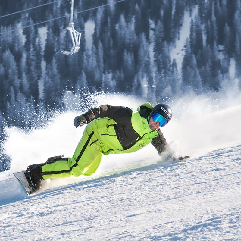 Snowboardlehrer von Snow Experts meistert eine dynamische Kurve bei hoher Geschwindigkeit während einer Abfahrt im Skigebiet KitzSki.