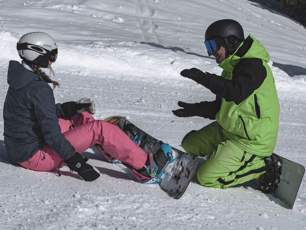 Snowboardlehrer erklärt einer Schülerin, wie sie ihre Balance auf dem Board hält, während des Unterrichts im Skigebiet KitzSki.