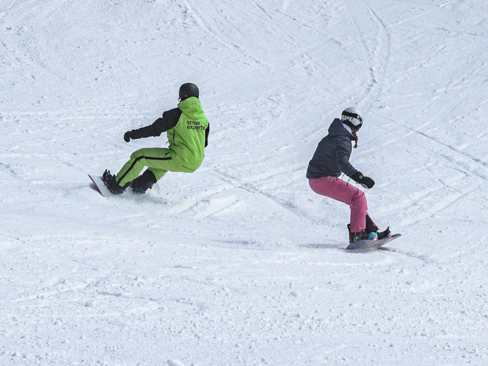 Snowboardlehrer mit Schülerin im Skigebiet KitzSki beim Privatunterricht auf den Pisten der Kitzbüheler Alpen.